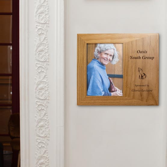 Red Alder Picture Frame With Old Woman Photo And Engraved With Prayer Hands And Youth Group Sponsorship Details On White Wall