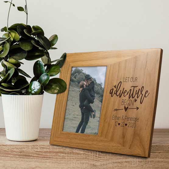Red Alder Picture Frame With Couple Photo And Engraved With Names And Date And Let Our Adventure Begin On Dresser With Plant