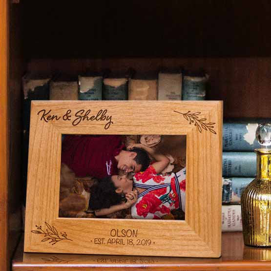 Red Alder Picture Frame With Couple Photo And Engraved With Names And Date And Leaves Art On Wood Bookshelf With Books