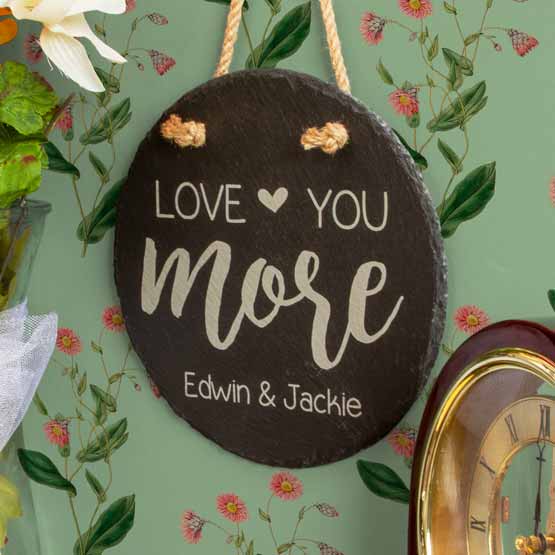 Custom Circle Slate Sign With Printing Of Love You More And Couple Names Hanging Via Rope On Wall With Flower Artwork
