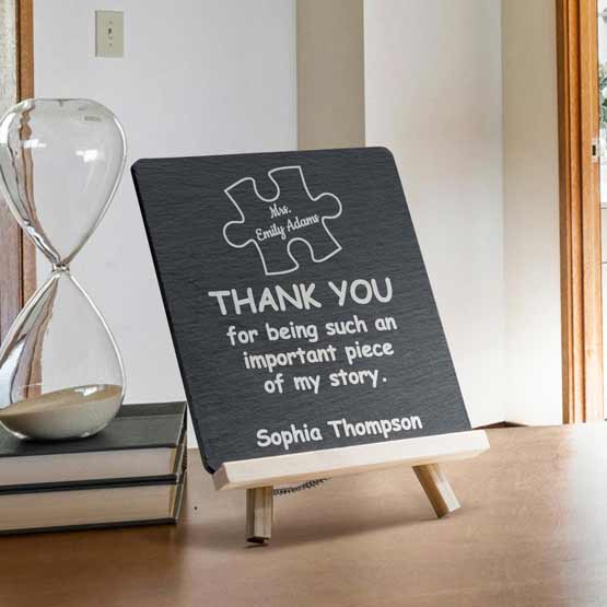 Slate Sign Printed With Teacher Appreciation Message And Puzzle Piece Art Standing On Shelf With Books Via Wooden Easel