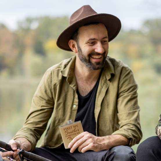 Man Fishing In Boat Outdoors And Holding Custom Leather Wrapped Stainless Steel Flask Laser Engraved With Brother Message