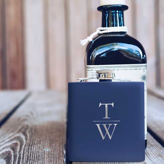Navy Blue Powder Coated Stainless Steel Flask Laser Engraved With The Letter T And L Standing On Wood Table With Bottle