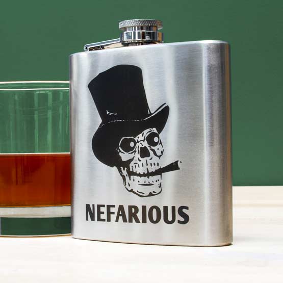 Custom Stainless Steel Flask Laser Fused With Nefarious And Skull In Top Hat Artwork On A White Shelf Beside Soy Candle