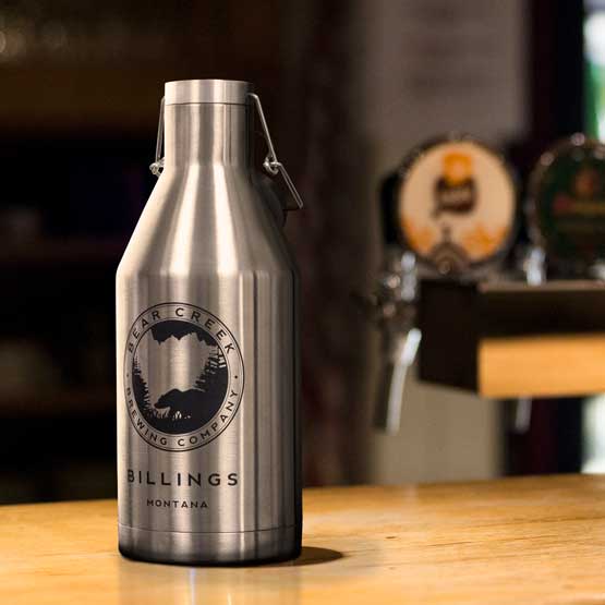 Stainless Steel Beer Growler With Swing Top Lid And Engraved With Brewing Company Logo And Location On A Wood Table Indoors