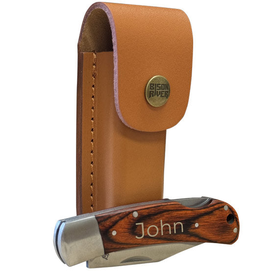 Custom Stainless Steel Folding Knife With Wood Handle Engraved With Name In A Closed Position Beside A Buckled Leather Sheath