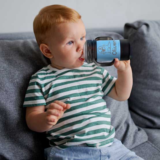 Child On Couch Drinking From Custom Light Blue Stainless Steel Sippy Cup With Handles And Engraved With Name And Cute Clipart