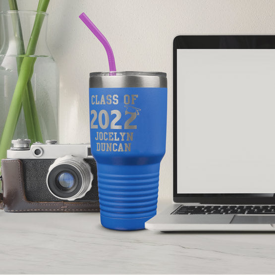 Blue 30 Ounce Tumbler With Straw And Engraved With Class Of 2022 Text And Student Name On White Desk With Camera And Laptop