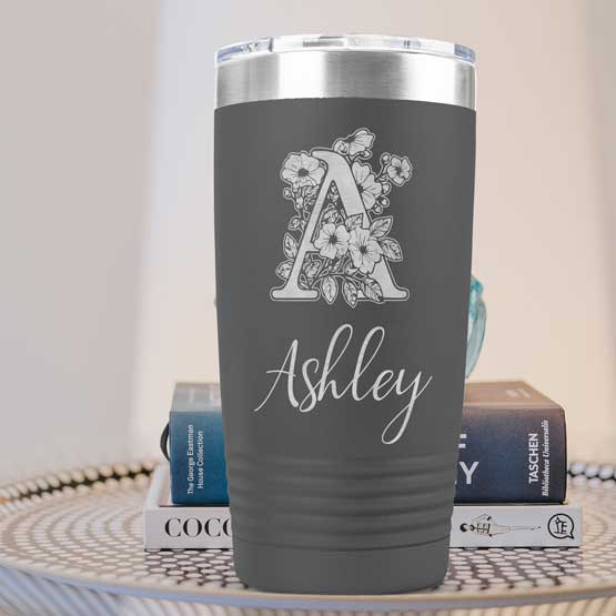 Custom Gray Twenty Ounce Stainless Steel Coffee Tumbler Engraved With Ashley And Monogram And Flower Art On Table With Books