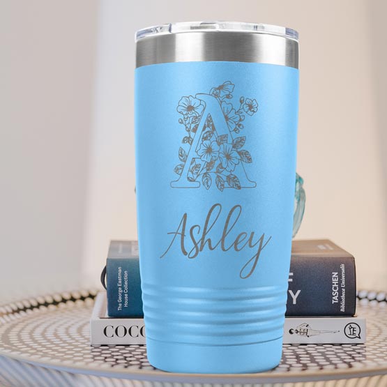 Light Blue Twenty Ounce Stainless Steel Coffee Tumbler Engraved With Ashley And Monogram And Flower Art On Table With Books