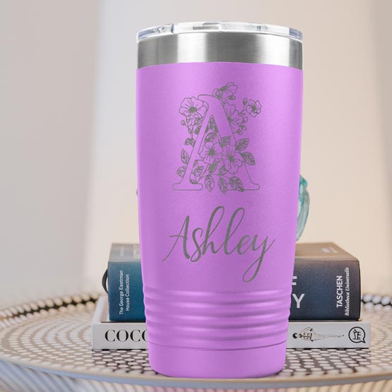 Light Purple Twenty Ounce Stainless Steel Coffee Tumbler Engraved With Ashley And Monogram And Flower Art On Table With Books