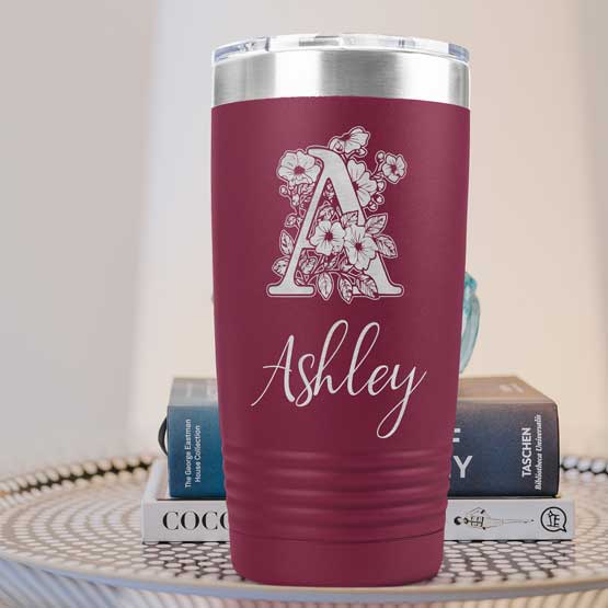 Maroon Twenty Ounce Stainless Steel Coffee Tumbler Engraved With Ashley And Monogram And Flower Art On Table With Books