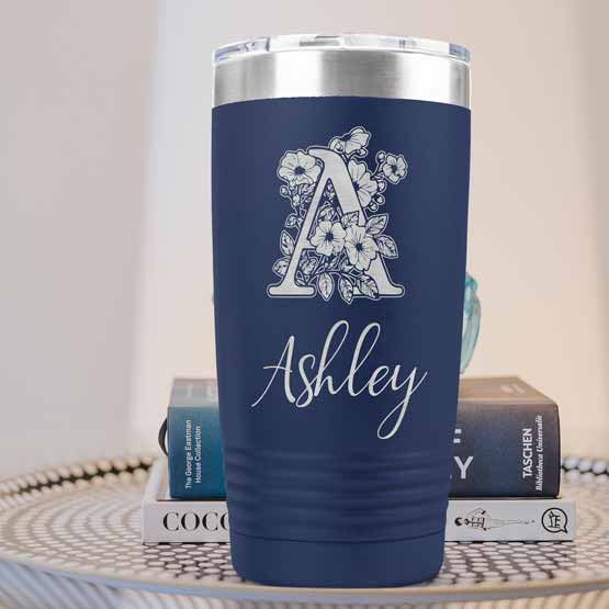 Navy Blue Twenty Ounce Stainless Steel Coffee Tumbler Engraved With Ashley And Monogram And Flower Art On Table With Books
