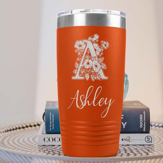 Orange Twenty Ounce Stainless Steel Coffee Tumbler Engraved With Ashley And Monogram And Flower Art On Table With Books