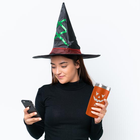 Woman In Witch Costume Holding Phone And Orange 20 Ounce Tumbler Engraved With Jack O Lantern Pumpkin Face Art And Name