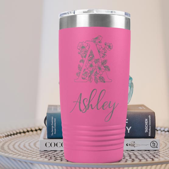 Pink Twenty Ounce Stainless Steel Coffee Tumbler Engraved With Ashley And Monogram And Flower Art On Table With Books