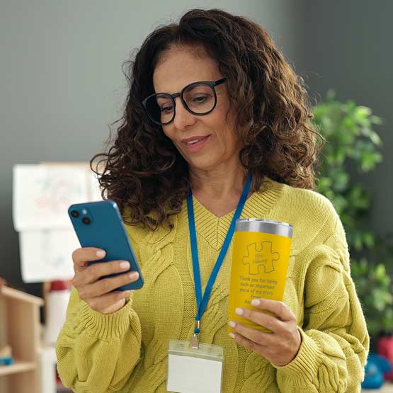 Woman Holding Phone And Yellow 20 Ounce Tumbler Engraved With Teacher Name Inside Puzzle Piece And Thank You Message