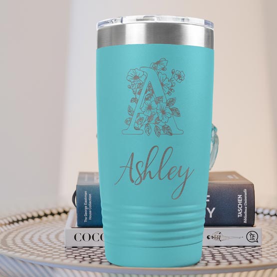 Teal Twenty Ounce Stainless Steel Coffee Tumbler Engraved With Ashley And Monogram And Flower Art On Table With Books