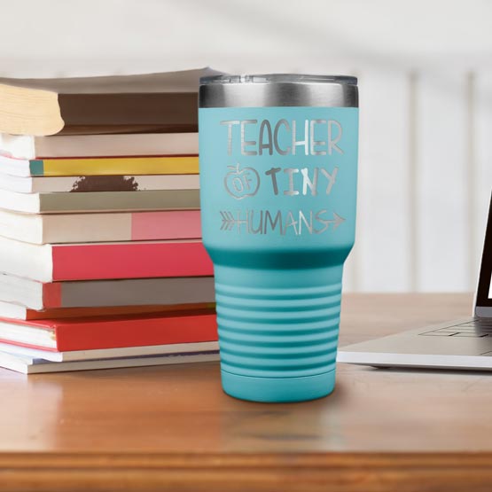Teal 30 Ounce Tumbler Laser Engraved With Teacher Of Tiny Humans Text And Apple Art On Desk With Books And Laptop