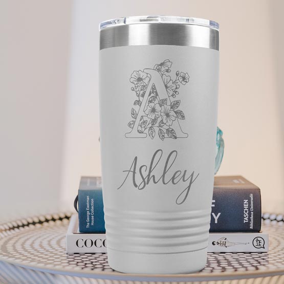 White Twenty Ounce Stainless Steel Coffee Tumbler Engraved With Ashley And Monogram And Flower Art On Table With Books