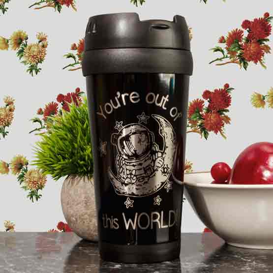 Black Travel Mug Engraved With Astronaut Art And You’re Out Of This World Message On Kitchen Counter By Plant And Food Bowl