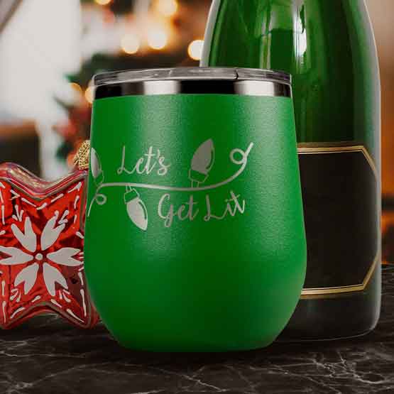 Green 12 Ounce Stemless Wine Tumbler Engraved With Christmas Lights Art And Let’s Get Lit Text On Table With Wine Bottle