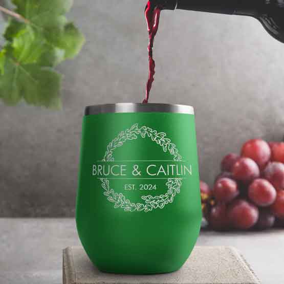 Wine Bottle Pouring Wine Into Green Stemless Wine Tumbler Engraved With Couple Names And Wheat Art On A Kitchen Counter