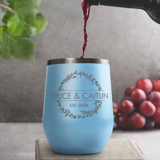 Wine Bottle Pouring Wine Into Light Blue Stemless Wine Tumbler Engraved With Couple Names And Wheat Art On A Kitchen Counter