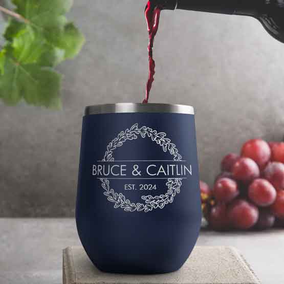 Wine Bottle Pouring Wine Into Navy Blue Stemless Wine Tumbler Engraved With Couple Names And Wheat Art On A Kitchen Counter