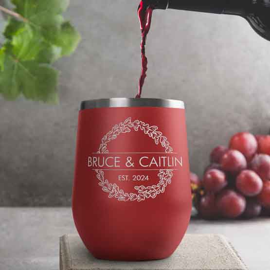 Wine Bottle Pouring Wine Into Red Stemless Wine Tumbler Engraved With Couple Names And Wheat Art On A Kitchen Counter