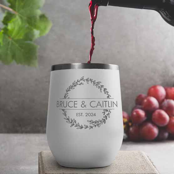 Wine Bottle Pouring Wine Into White Stemless Wine Tumbler Engraved With Couple Names And Wheat Art On A Kitchen Counter