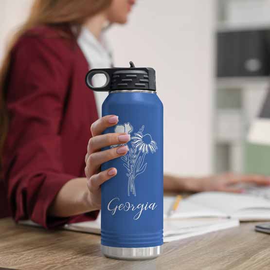 Woman At Office Desk Holding Blue Thirty Two Ounce Water Bottle With Straw And Laser Engraved With Name And Flower Art