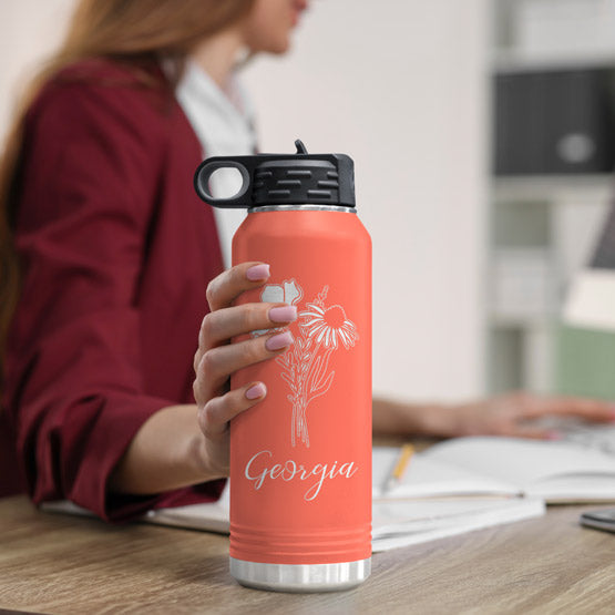 Woman At Office Desk Holding Coral Thirty Two Ounce Water Bottle With Straw And Laser Engraved With Name And Flower Art
