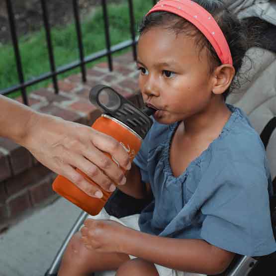 Hand Serving Orange Stainless Steel Child Water Bottle With Straw And Engraved Name To Little Girl In Stroller Outdoors
