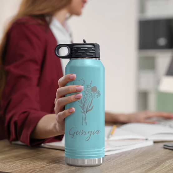 Woman At Office Desk Holding Teal Thirty Two Ounce Water Bottle With Straw And Laser Engraved With Name And Flower Art