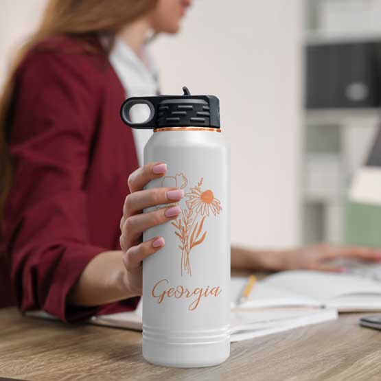 Woman At Office Desk Holding White And Rose Gold Thirty Two Ounce Water Bottle With Straw And Engraved Name And Flower Art