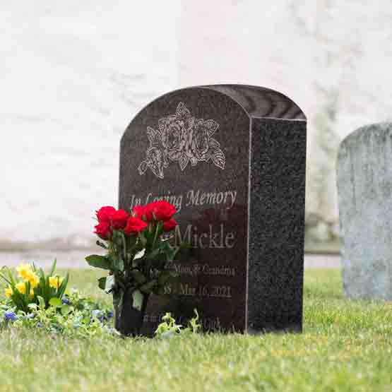 Flowers Beside Granite Tombstone Engraved With Flower Art And Memorial Message For Betty Mickle Standing In Cemetery