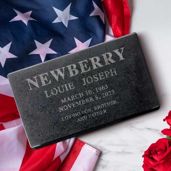 Rectangle Shaped Granite Headstone Engraved With Memorial Details On Marble Counter With Flowers And United States Flag