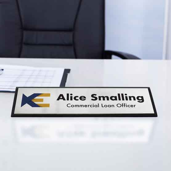 Desk Wedge With Black Piano Finish And Silver Plate Printed With Logo And Employee Details On White Office Desk With Papers