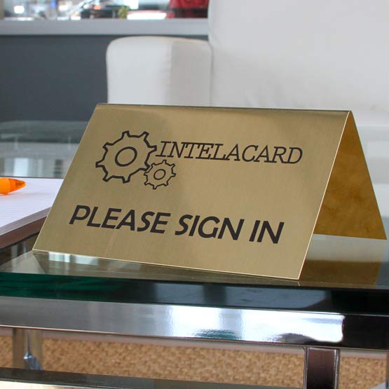 Custom Engraved Brass Table Tent Name Plate On Glass Table Near Notebook.