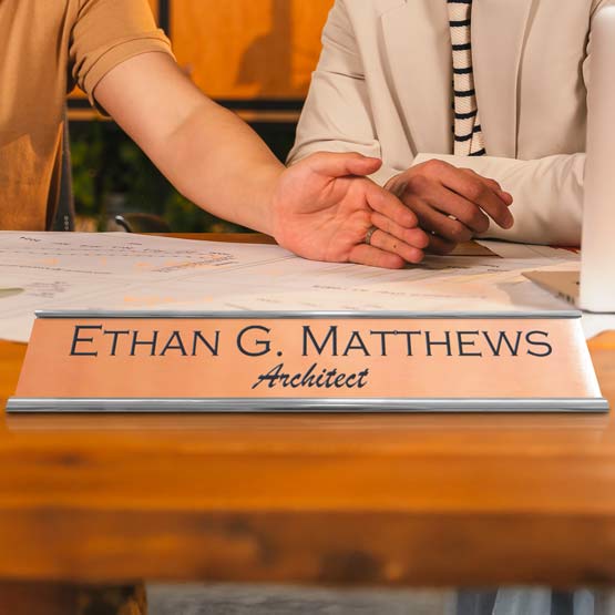 Custom Engraved Copper Desk Name Plate Near Building Plans On Desk.