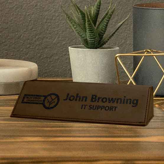 Dark Brown Faux Leather Desk Wedge Laser Engraved With Logo And Employee Details On Wood Desk With Plant And Decor