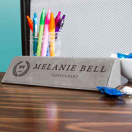 Gray Faux Leather Desk Wedge Laser Engraved With Logo And Employee Details On Wood Desk With Jar Of Pens