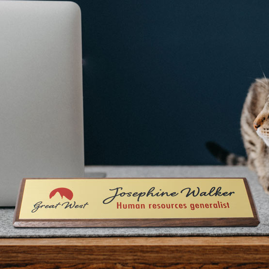 Walnut Desk Wedge With Gold Aluminum Plate Printed With Logo And Employee Details On Work Desk With Computer And Cat