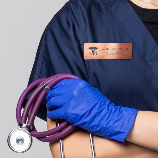 Nurse Wearing Blue Gloves And Holding A Stethoscope While Wearing A Custom Copper Medical Name Tag. 
