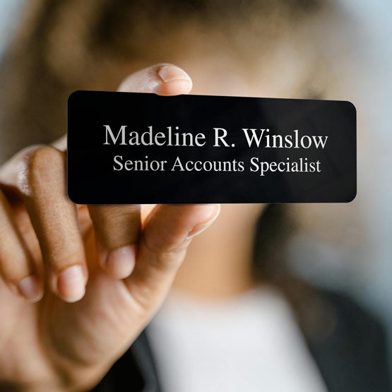 Woman Holding Up Custom Black Magnetic Name Badge Laser Engraved With Name And Senior Accounts Specialist Text In White