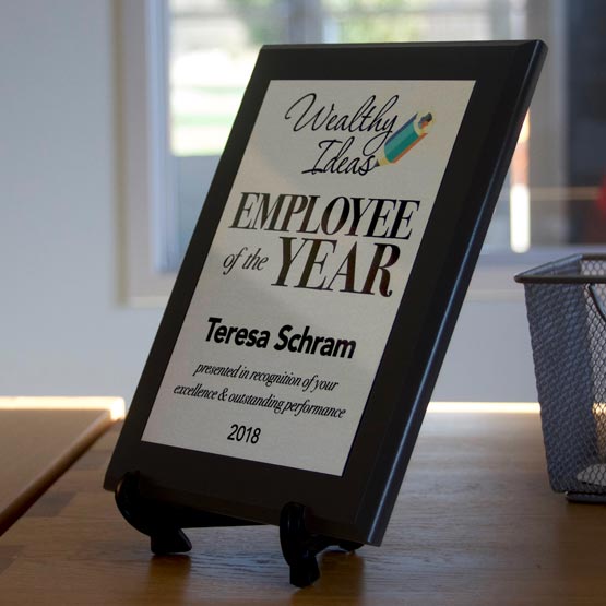 Personalized Employee Of The Year Plaque With Easel On Wooden Desk Near Metal Basket.