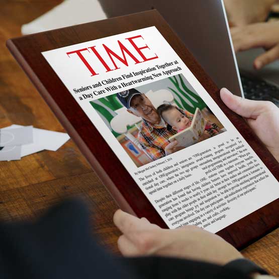 Man Holding Custom Newspaper Plaque With Article Near Laptop Computer And Cards.