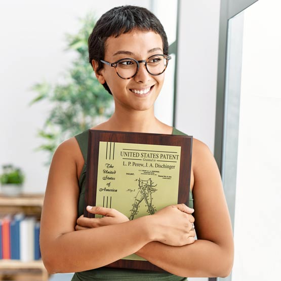 Custom Aluminum Patent Plaque With Wood Board, Seal, And Ribbon On Left Side Of Plate Held By Happy Woman