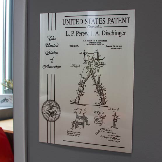 Custom Silver Aluminum Wall Patent Plaque With Patent Details And Seal And Ribbon Hanging On Wall Beside Office Door
